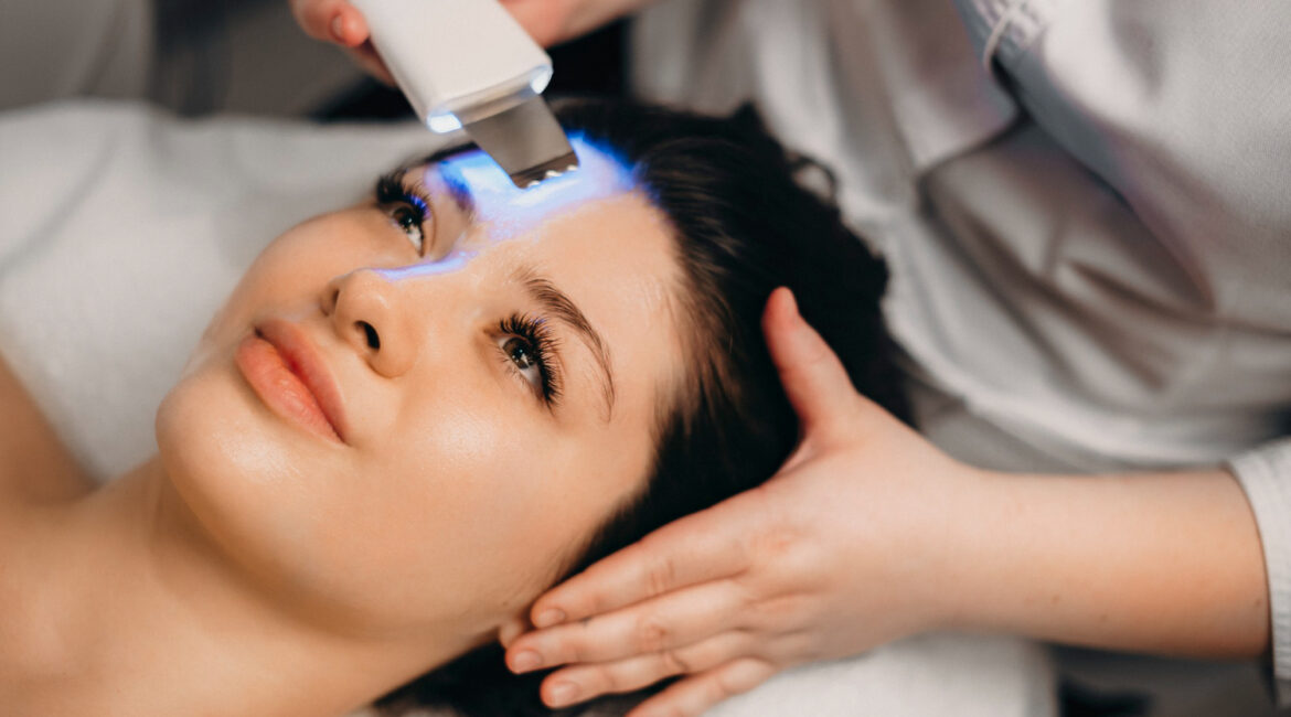 close up portrait beautiful female brunette laying with eyes open spa bed while having ultrasound procedures her face by female cosmetologist